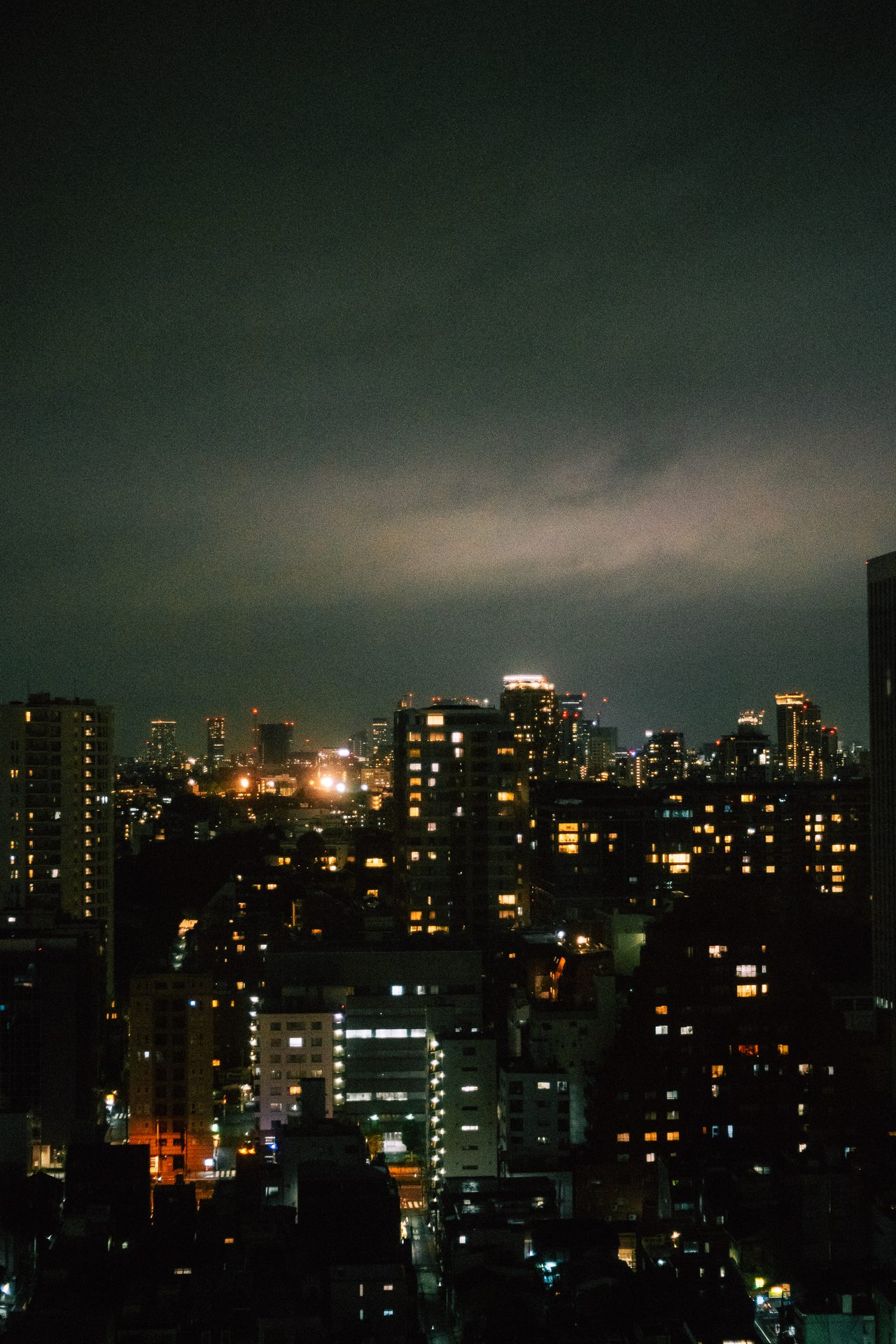 Glowing city windows beneath heavy dark storm clouds.